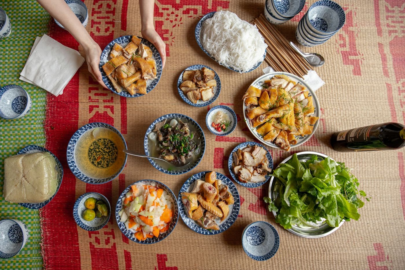 Mâm cơm gia đình trải trên chiếu, nhiều đĩa thức ăn, bát nước chấm và rau sống